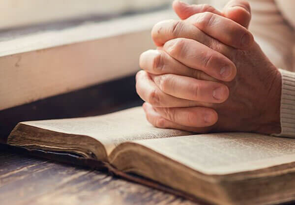Hands folded over open Bible